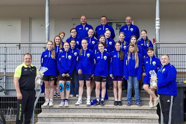 Gruppenfoto einer Jugendmannschaft in blauen Trainingsjacken, umgeben von Trainern, auf einer Treppe.